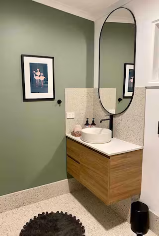 Powder room with terrazzo tiling, timber vanity and oval mirror