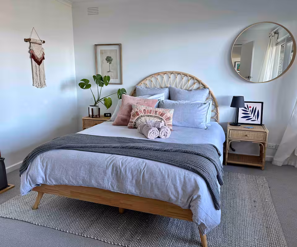 Primary bedroom with rattan bedhead, linen bedding and round mirror